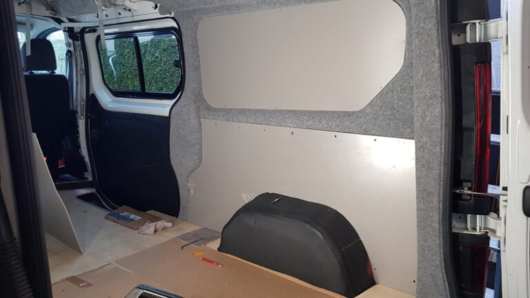 Vue intérieure d'un Renault trafic L2H1 en cours d'aménagement. Les parois latérales sont recouvertes d'une moquete grise avec des panneaux Pvc de la gamme Komatex. Aménagement et habillage en cours.