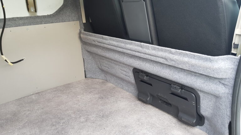 Vue intérieure d'un Renault trafic L2H1 en cours d'aménagement. Les parois latérales sont recouvertes d'une moquete grise avec des panneaux Pvc de la gamme Komatex. La partie basse de la cloison de séparation a été moquetté. Aménagement et habillage en cours.