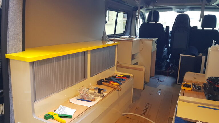 Intérieur d'un Renault trafic L2H1 en cours de transformation en camping-car, avec outils, étagères et meubles partiellement assemblés.