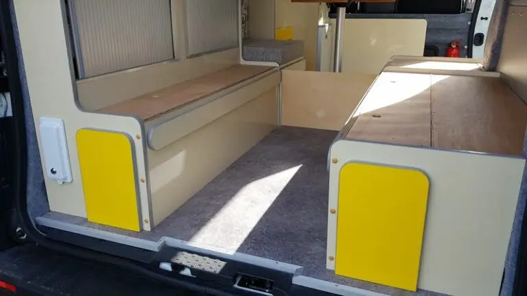 Intérieur d'un Renault trafic L2H1 aménagé en camping-car (VASP). Il y a un petit coin cuisine avec des meubles de rangement. Le sol est recouvert d'un linoléum gris.