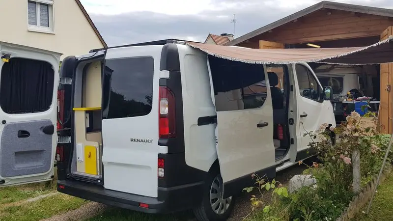 Renault trafic L2H1 blanc avec porte coulissante latérale, portes arrière ouverte et un auvent en toile.